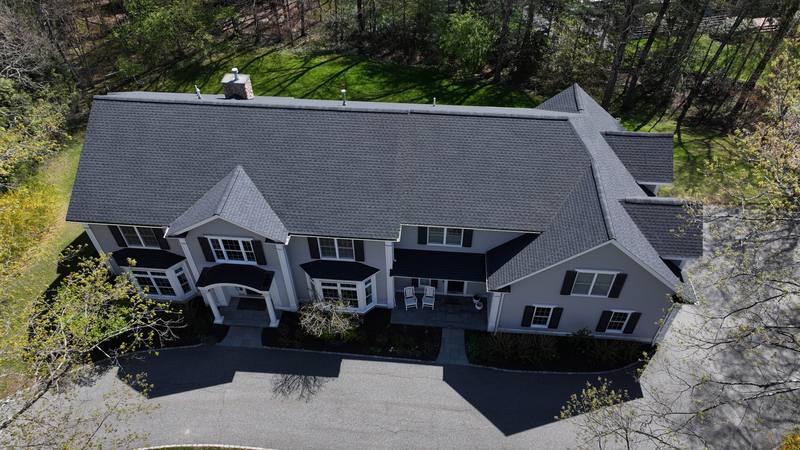 Wide colonial with a dark shingle roof and bay windows